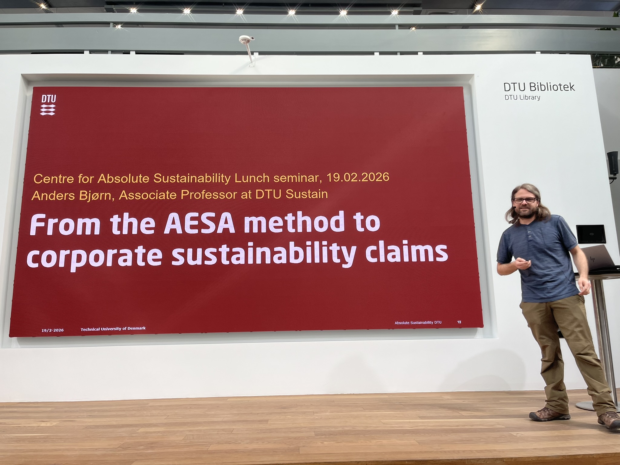 A main stands in front of a presentation screen that reads "From the AESA method to corporate sustainability claims"
